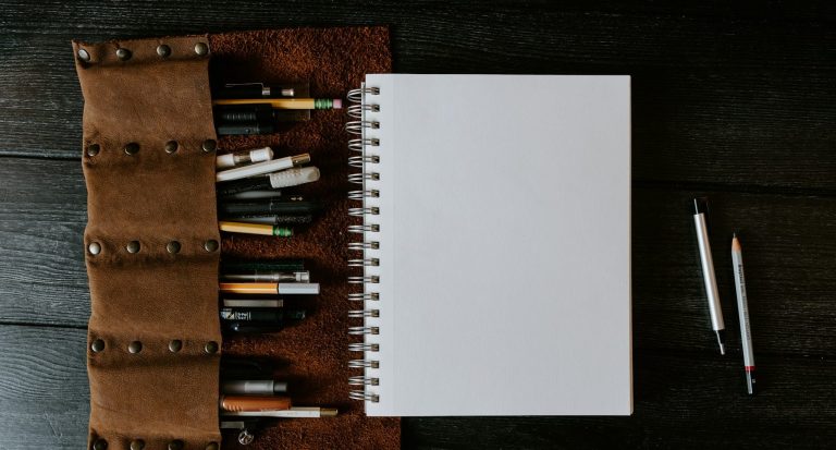A blank notepad ready for bid writing brainstorming with pens and pencils on a brown leather holder.