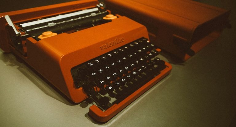 Retro orange typewriter on a dark surface, ready to type a bid document, angled view showing keys and carriage.