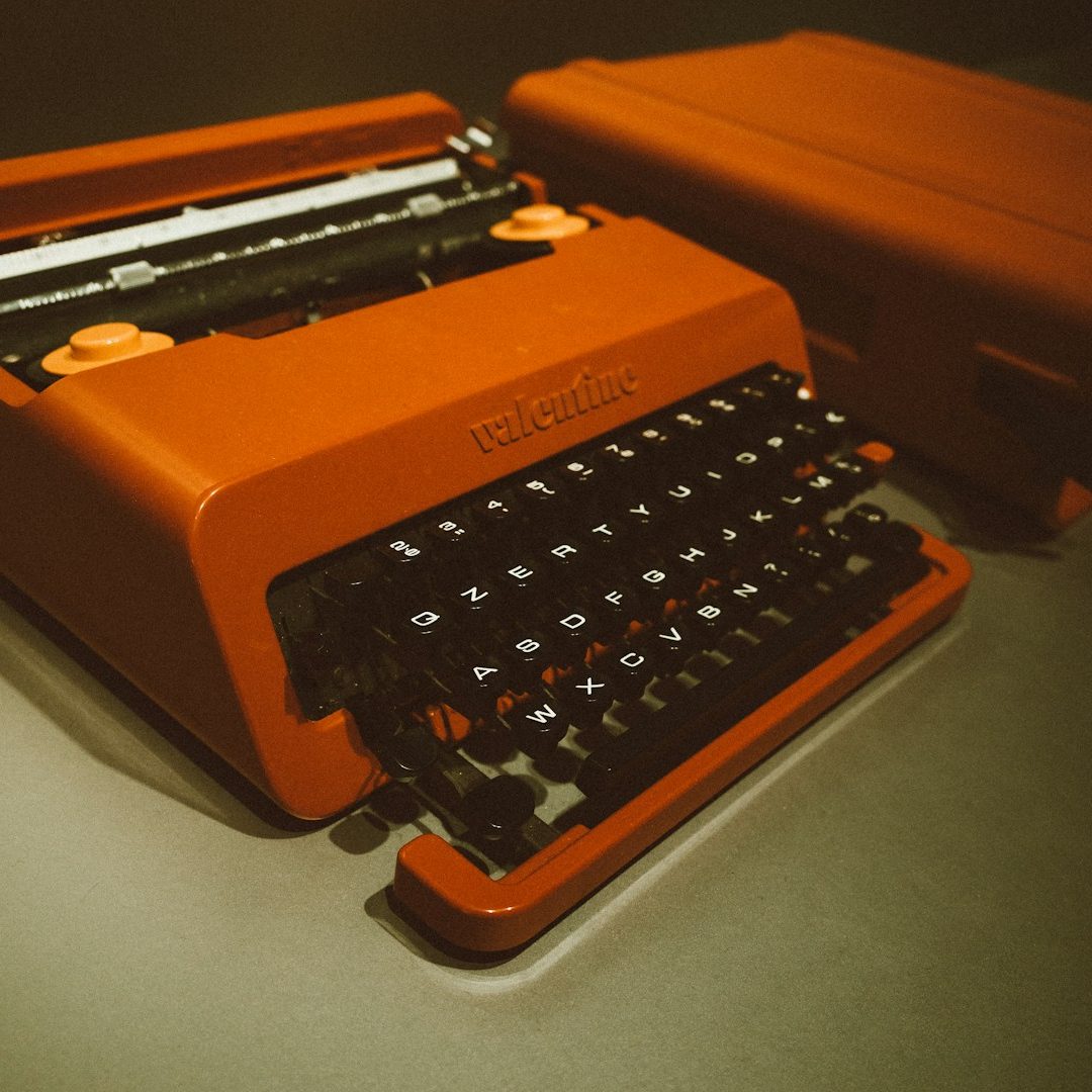 Typewriter A vibrant orange typewriter for bid writing with black keys, partially open lid.