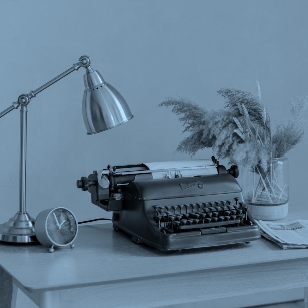 Vintage Typewriter Vintage typewriter on a wooden desk, ready to write a bid, with a lamp, clock, and dried plants in a vase.