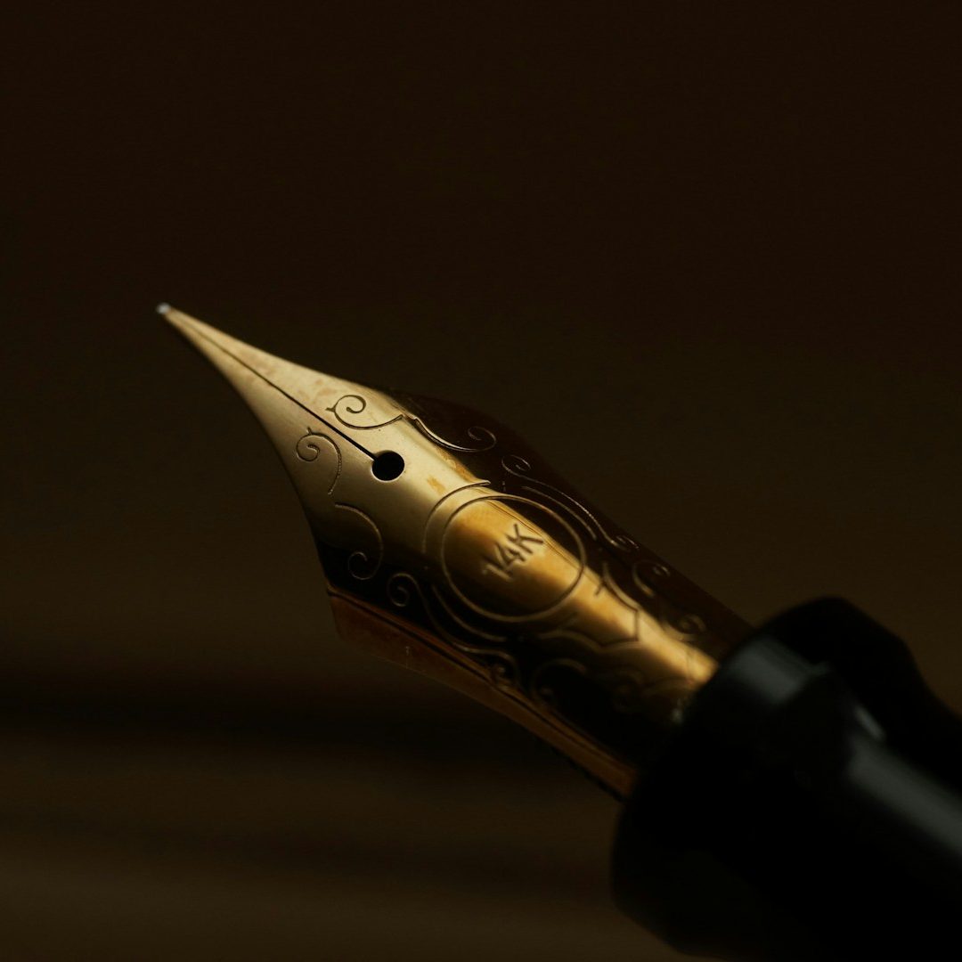 Close-up of a bid writer's gold fountain pen nib on a dark background.